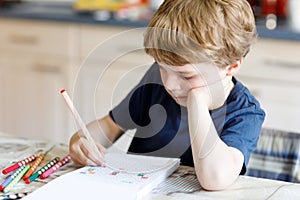 Tired sad and drepressed little kid boy at home making homework at the morning before the school starts. Little child
