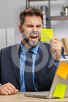 Tired sad exhausted businessman working on laptop at office with many sticker tasks, panic attack