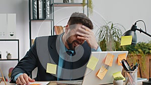 Tired sad exhausted businessman working on laptop at office with many sticker tasks, panic attack