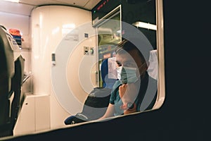 Tired and sad male passenger sits in face shield and looks through the window. View through the window. Topic passenger public