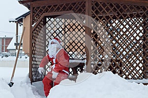 Tired santa claus sitting on wooden chair after work of snow rem