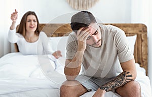 Tired of scandals. Young woman swears, sad man holds his head with hand and sits on bed