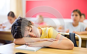 Tired school boy sleeping in classroom during lesson
