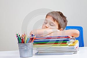 Tired school boy sleeps sitting at the table with big pile of books, textbooks and notebooks