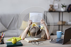 Tired school girl sleeping at table holding paper