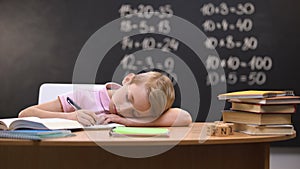 Tired schoolboy napping on desk, fallen asleep while preparing assignment