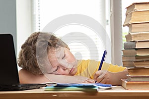 Tired schoolboy sitting at table doing homework