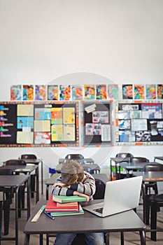 Tired schoolboy sleeping on stack of book sitting in classroom