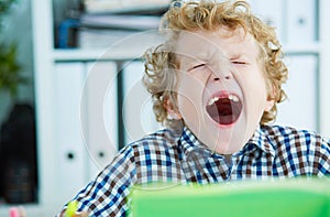 Tired schoolboy yawn sitting at the table in class at the lesson.