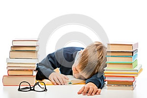 Tired schoolchild is sleeping at a table between piles of books