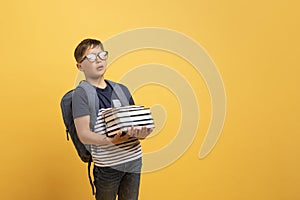 Tired schooler boy carrying books, isolated on yellow