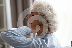 Tired senior grandma rubbing stiff neck suffering from fibromyalgia pain photo