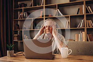 Tired senior man having a headache in library after using the computer