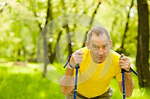 Tired senior man making nordic walking in the park