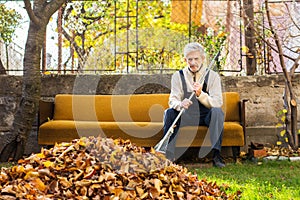 Tired man taking rest from cleaning fallen autumn leaves in the