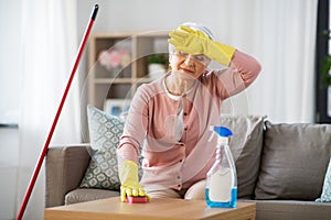 Tired senior woman cleaning table at home