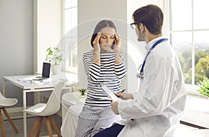 Tired senior woman complains to doctor of severe headaches during visit or consultation at clinic.