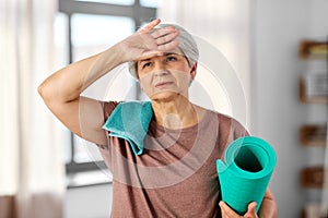 tired senior woman with yoga mat and towel