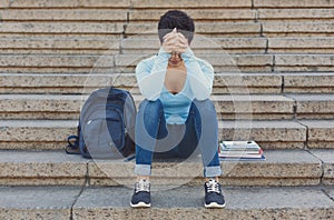 Tired shorthaired student girl sitting on the steps outdoors