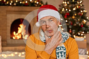 Tired or sick old man in Santa Claus hat, touching neck feeling pain and fever, getting ill on Christmas holiday, posing on