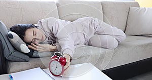 Tired sleeping woman hides ringing alarm clock under pillow