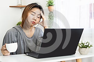 Tired and sleepy Asian woman worker drinking coffee caused by overworked from home office