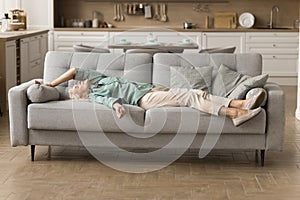 Tired sleepy blonde elderly woman in shoes resting on couch