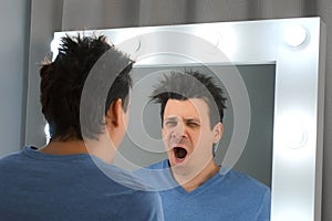 Tired sleepy man with a hangover looks in the mirror yawns in the morning.