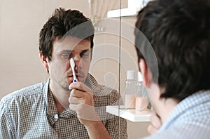 Tired sleepy man with a hangover who has just woken up brush his teeth, looks at his reflection in the mirror.