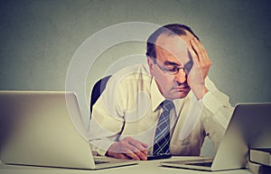 Tired sleepy man sitting at desk with books in front of two laptop computers