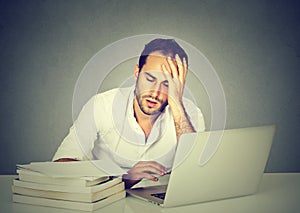 Tired sleepy man sitting at desk with books laptop computer