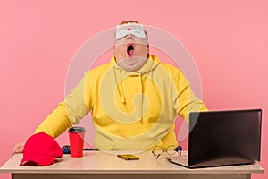 Tired sleepy man sitting at desk with coffee in front of laptop computer