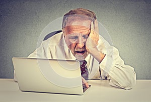 Tired sleepy senior man sitting at his desk in front of laptop computer