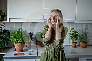 Tired sleepy woman feeling headache rubbing temples feeling dizziness standing on kitchen at home.