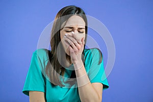 Tired sleepy woman yawns, covers her mouth with hand. Very boring, uninteresting. Violet studio background.