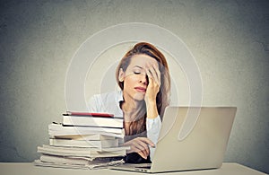 Tired sleepy young woman sitting at her desk with books in front of computer