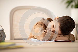 Tired small european boy lies at table sleeping, resting from lesson in school room interior