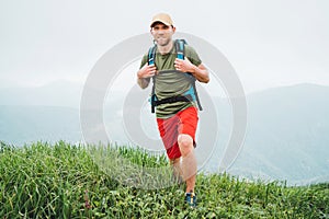 Tired smiling hiker man walking by the foggy cloudy weather mountain range path with backpack. Active sports backpacking healthy