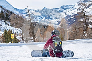 Tired snowboarder sitting on snow covered landscape while looking at mountains