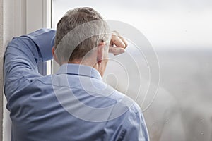 Tired or sorrowful businessman looking out of a window