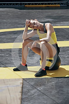 Tired sport woman resting on med ball after training outdoors