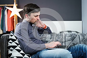 Tired strained man suffering from neck pain while working at computer. Male touchingly massages neck, puts on neck collar, sitting