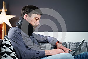 Tired strained man suffering from neck pain while working at computer. Male touchingly massages neck, puts on neck collar, sitting