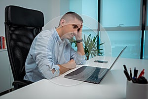Tired or stressed young businessman sitting in front of computer in office