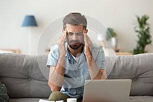 Tired stressed young man suffering from headache after computer work