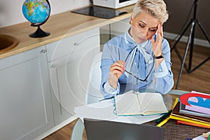 Tired stressed young teacher woman sitting at her desk with books in front laptop