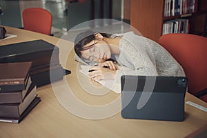 Tired student girl with glasses lying on books in library