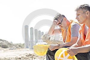 Tired supervisor sitting with colleague at construction site photo