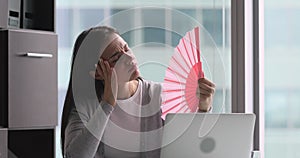 Tired sweaty businesswoman waving fan suffer from heat in office