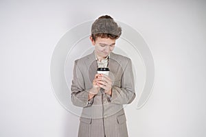 Tired teen boy in grey business suit with paper Cup of coffee in hand on white studio background